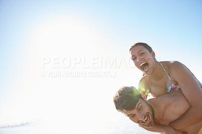 Buy stock photo Shot of a young man giving his girlfriend a piggyback on the beach