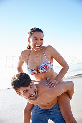 Buy stock photo Shot of a young man giving his girlfriend a piggyback on the beach