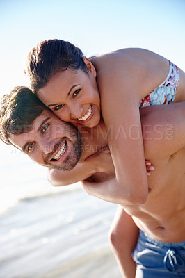 Buy stock photo Shot of a young man giving his girlfriend a piggyback on the beach