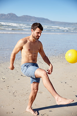 Buy stock photo Shot of a young man kicking a ball around on a beach