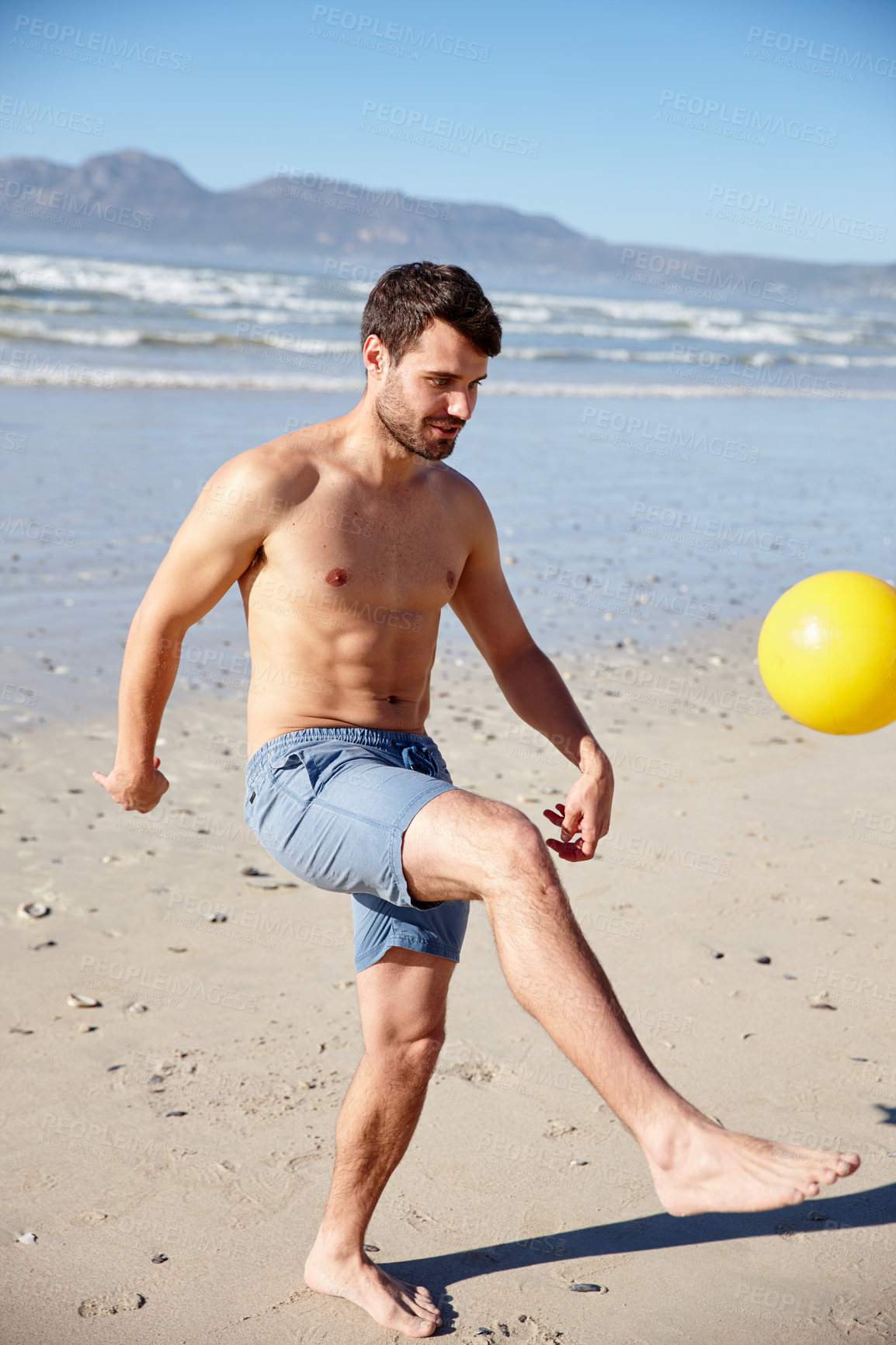 Buy stock photo Shot of a young man kicking a ball around on a beach