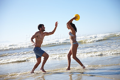 Buy stock photo Shot of a happy couple playing in the shallow water together on the beach