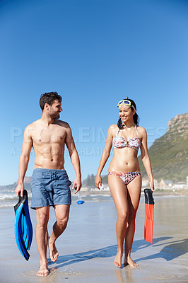 Buy stock photo Shot of a young couple walking along a beach together with snorkeling gear