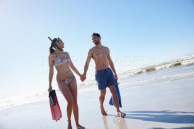 Buy stock photo Shot of a young couple walking along a beach together with snorkeling gear