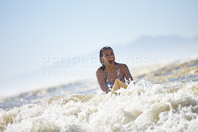 Buy stock photo Shot of and excited young woman riding a surfboard in the shallow waves