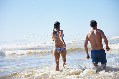 Buy stock photo Rearview of a young couple walking into the waves together