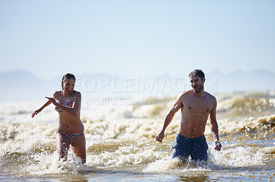 Buy stock photo Shot of a laughing young couple walking out of the surf together 