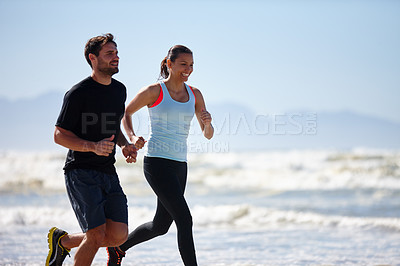 Buy stock photo Cropped shot of a young couple running along a beach together