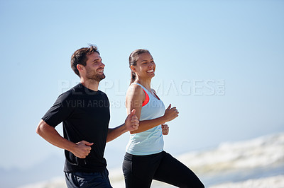 Buy stock photo Shot of a happy young couple running along a beach together