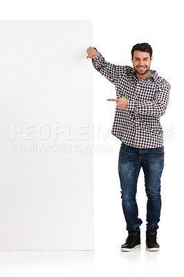 Buy stock photo Studio portrait of a handsome young man pointing towards the copyspace he's leaning on