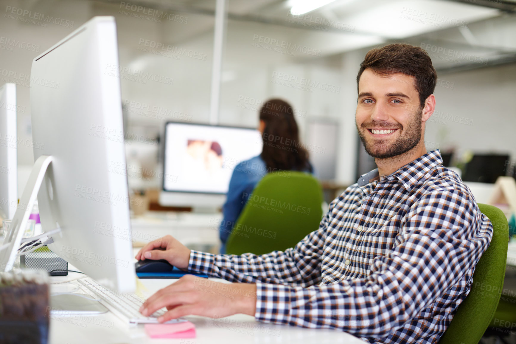 Buy stock photo Portrait of a handsome young designer sitting at his desk with a colleague in the background