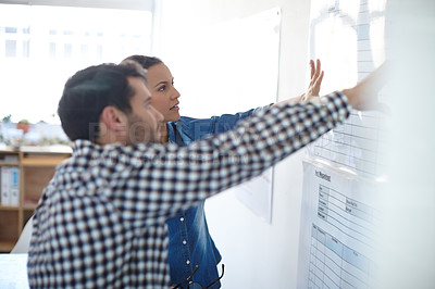 Buy stock photo Cropped shot of two colleagues discussing work at a whiteboard