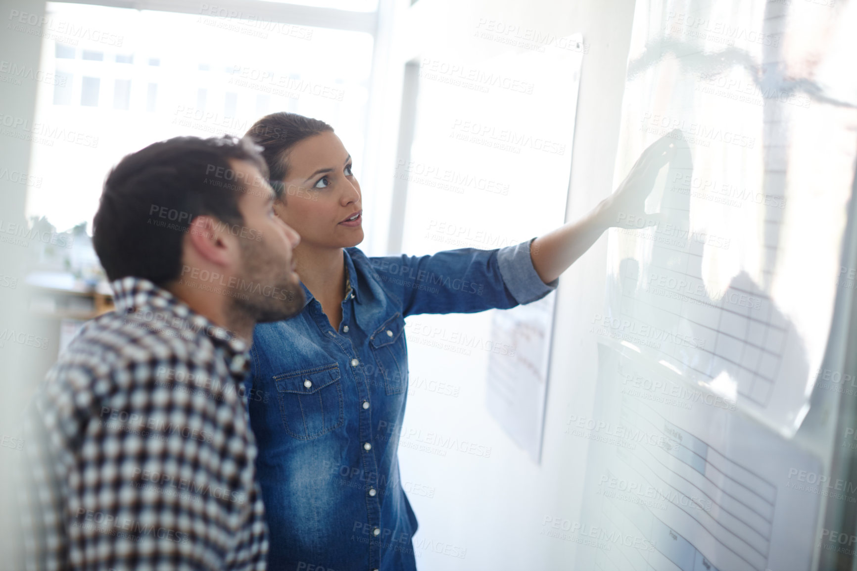 Buy stock photo Cropped shot of two colleagues discussing work at a whiteboard