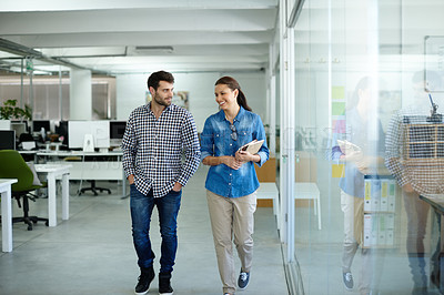 Buy stock photo Shot of two colleagues talking while walking in the office
