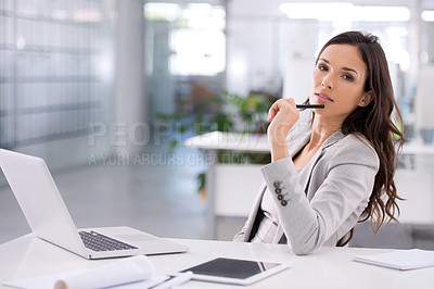 Buy stock photo Confident businesswoman thinking about a corporate strategy to boost sales at her desk while holding a pen with her laptop open in an office. Successful professional female planning a campaign alone