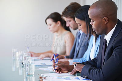 Buy stock photo Shot of a row of businesspeople taking notes during a work conference