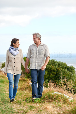 Buy stock photo Old couple, walking and holding hands in nature on holiday, vacation or support in retirement. Love, man and woman with conversation, care or happiness in marriage together on grass at beach or park