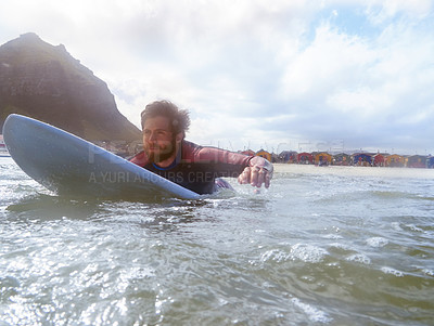 Buy stock photo Shot of a young male surfer paddling out on his surfboard