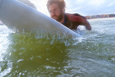 Buy stock photo Shot of a young male surfer paddling out on his surfboard