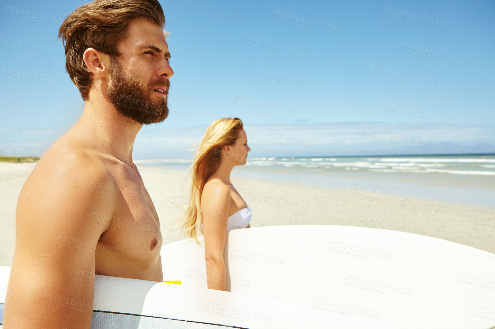 Buy stock photo Shot of a young couple walking on the beach, carrying their surfboards