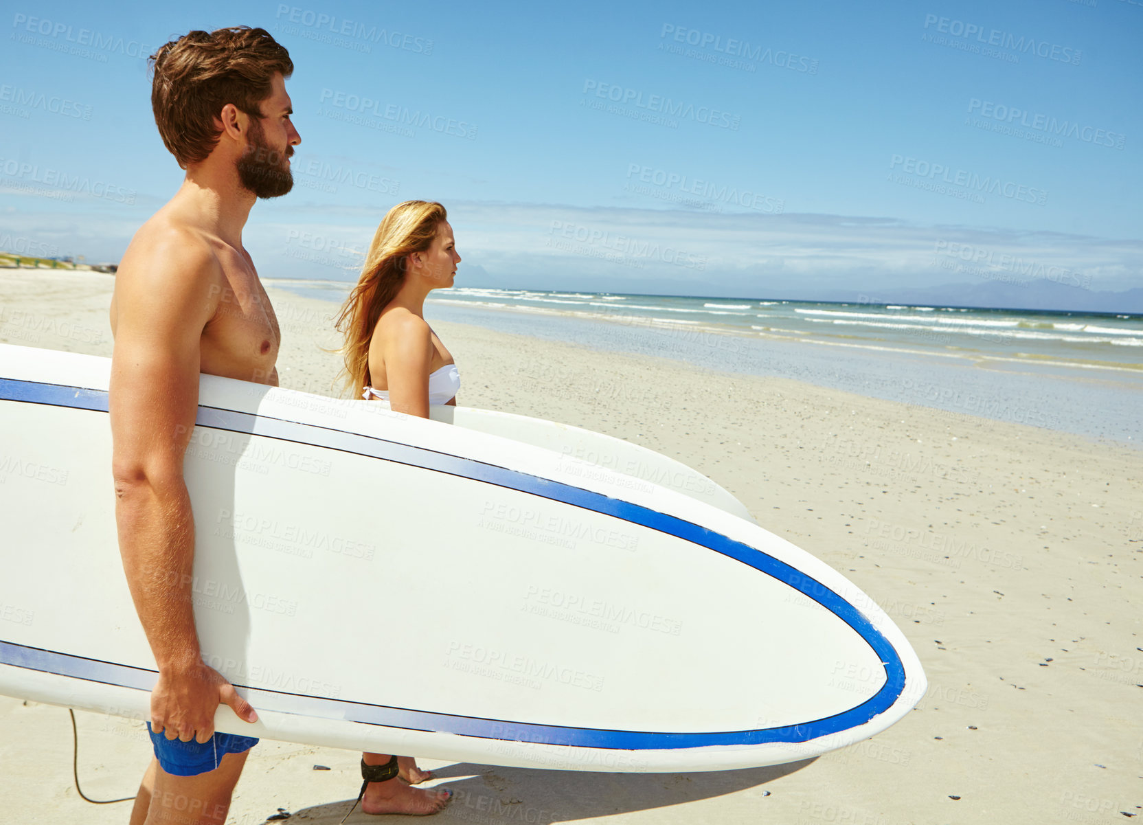 Buy stock photo Shot of a young couple standing on the beach with their surfboards looking out at the ocean