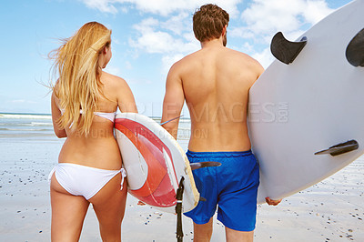 Buy stock photo Rearview shot of a young couple heading out into the ocean with their surfboards