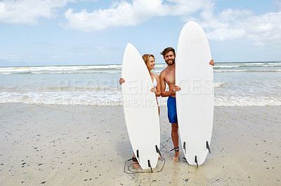 Buy stock photo Shot of a young couple standing alongside their surfboards on the beach