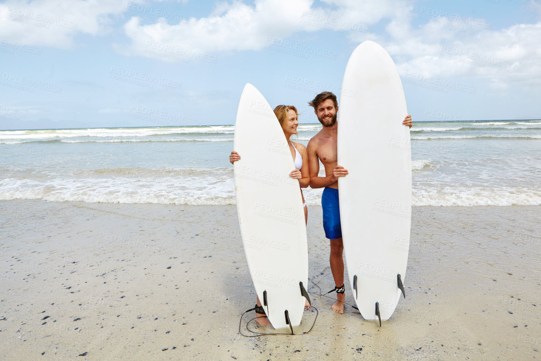 Buy stock photo Shot of a young couple standing alongside their surfboards on the beach