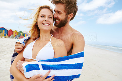 Buy stock photo Shot of an affectionate young couple standing wrapped in a towel on the beach