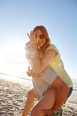 Buy stock photo Portrait of a handsome young man giving his girlfriend a piggyback at the beach