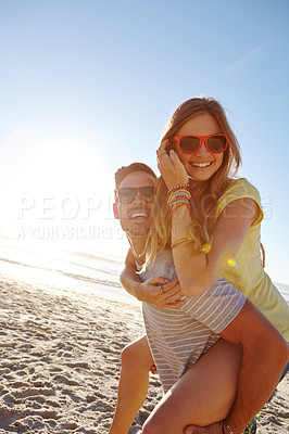 Buy stock photo Shot of a handsome young man giving his girlfriend a piggyback at the beach