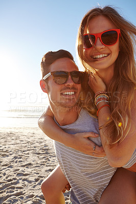 Buy stock photo Portrait of a handsome young man giving his girlfriend a piggyback at the beach