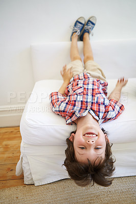 Buy stock photo Shot of an adorable little boy playfully hanging upside down on the edge of the sofa