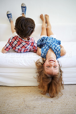 Buy stock photo Shot of a young brother and sister playfully hanging upside down on the edge of the sofa