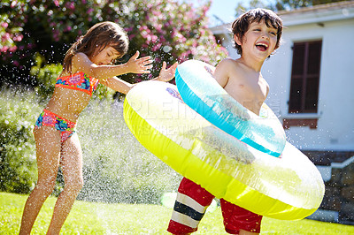 Buy stock photo Shot of a brother and sister having fun with a sprinkler in the backyard