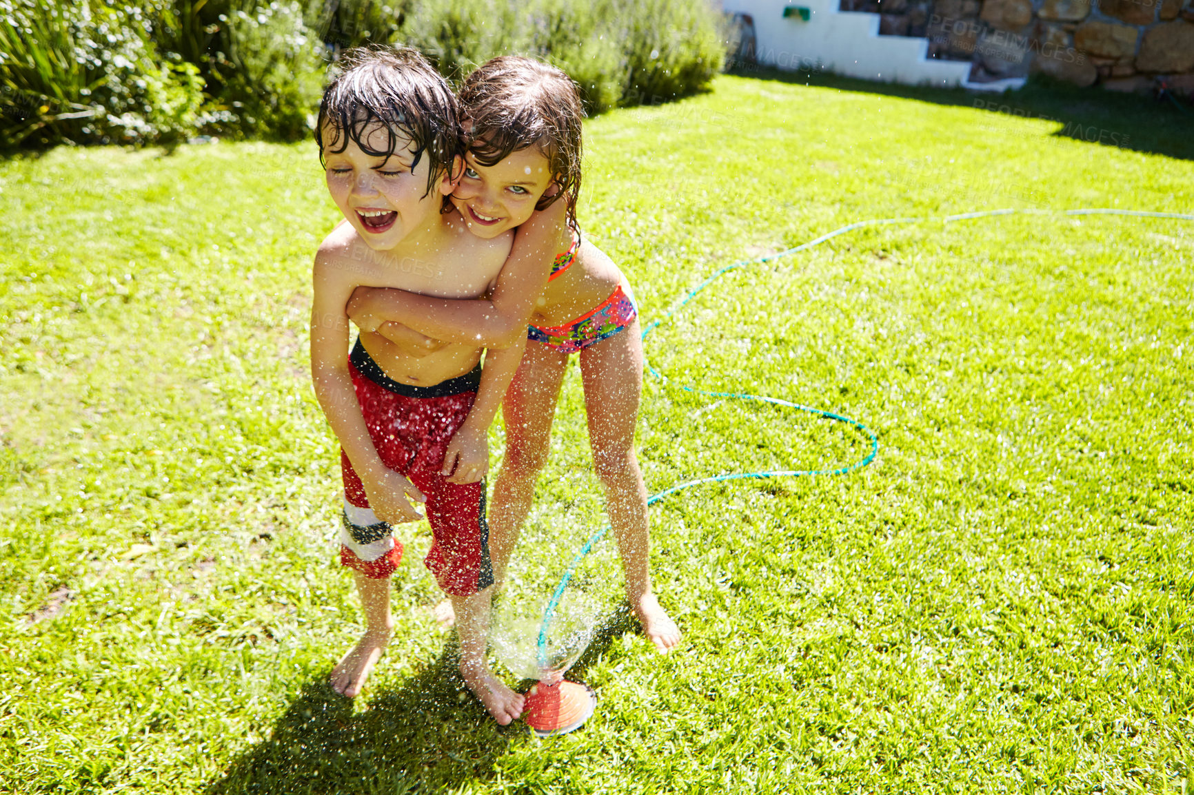 Buy stock photo Shot of a brother and sister having fun with a sprinkler in the backyard