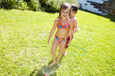 Buy stock photo Shot of a brother and sister having fun with a sprinkler in the backyard