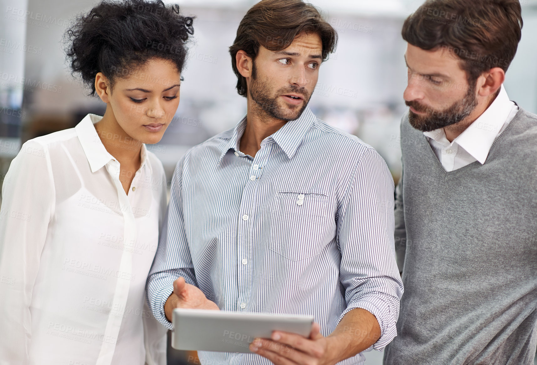 Buy stock photo Shot of three young businesspeople standing in his office and talking over a tablet