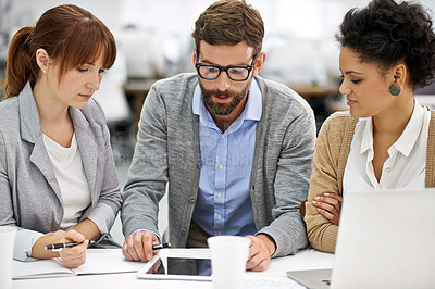 Buy stock photo Shot of a group of young office professionals talking over a digital tablet