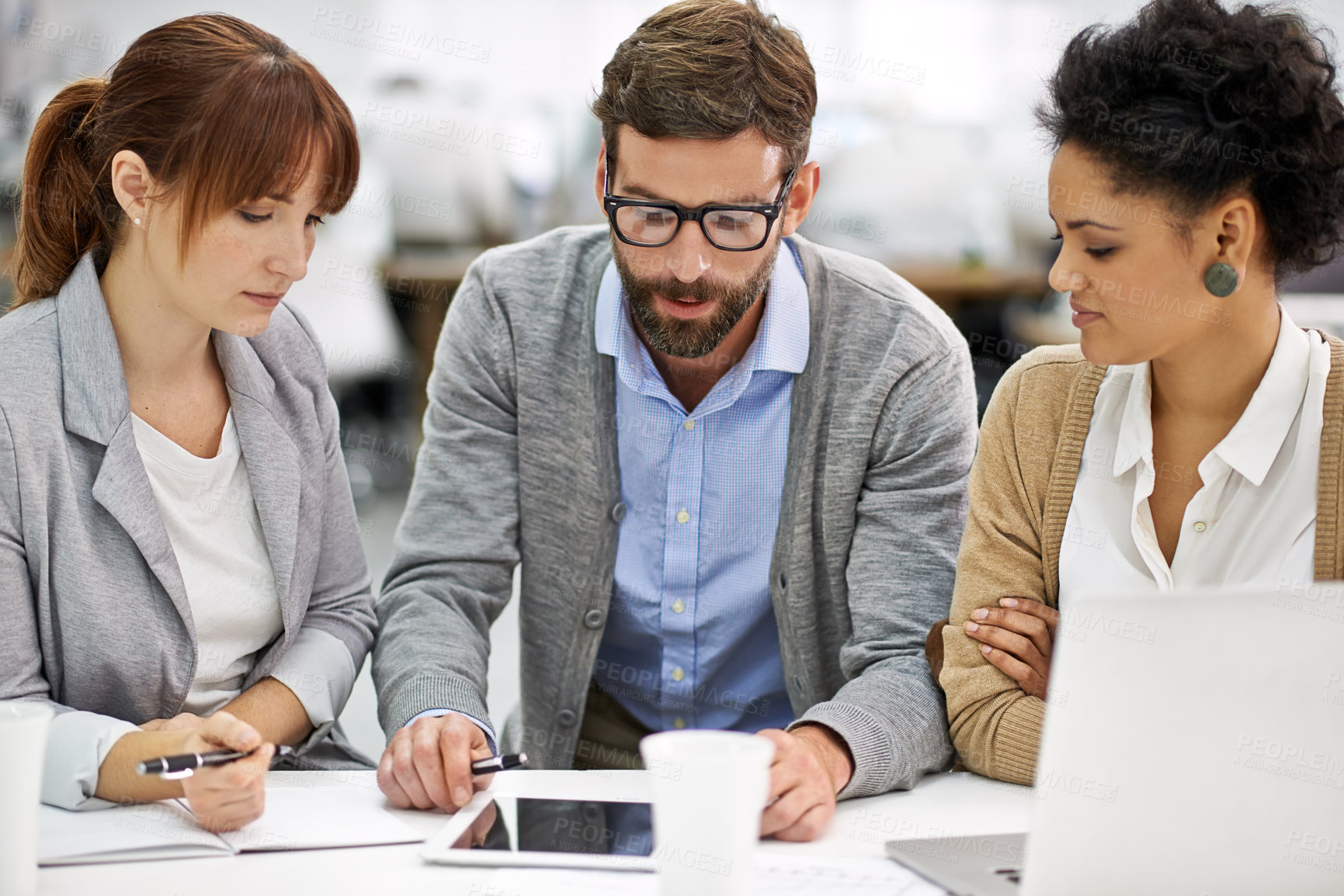 Buy stock photo Shot of a group of young office professionals talking over a digital tablet