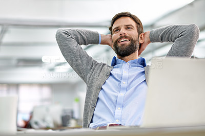 Buy stock photo Shot of a young businessman working on his laptop in the office and leaning back in his chair
