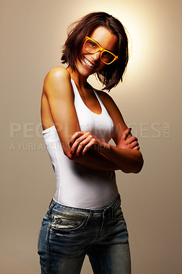 Buy stock photo Confident girl, glasses or smile in casual fashion eyewear as edgy, urban or street style in studio. Happy woman, specs or arms crossed in tank, jeans or mock up portrait on brown background