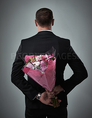 Buy stock photo Valentines day, surprise bouquet and flowers of a man in a suit with love present behind back. Flower gift, suit and male model in a isolated gray background studio feeling romantic for a formal date