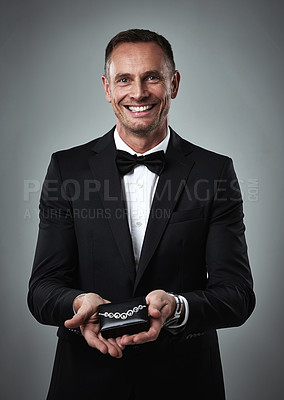 Buy stock photo Jewelry, smile and portrait of a man giving a valentines present in a studio. Isolated, gray background and happy person in a suit with happiness holding a necklace gift feeling love and classy