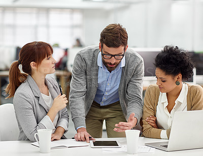 Buy stock photo Shot of a group of young office professionals talking over a digital tablet