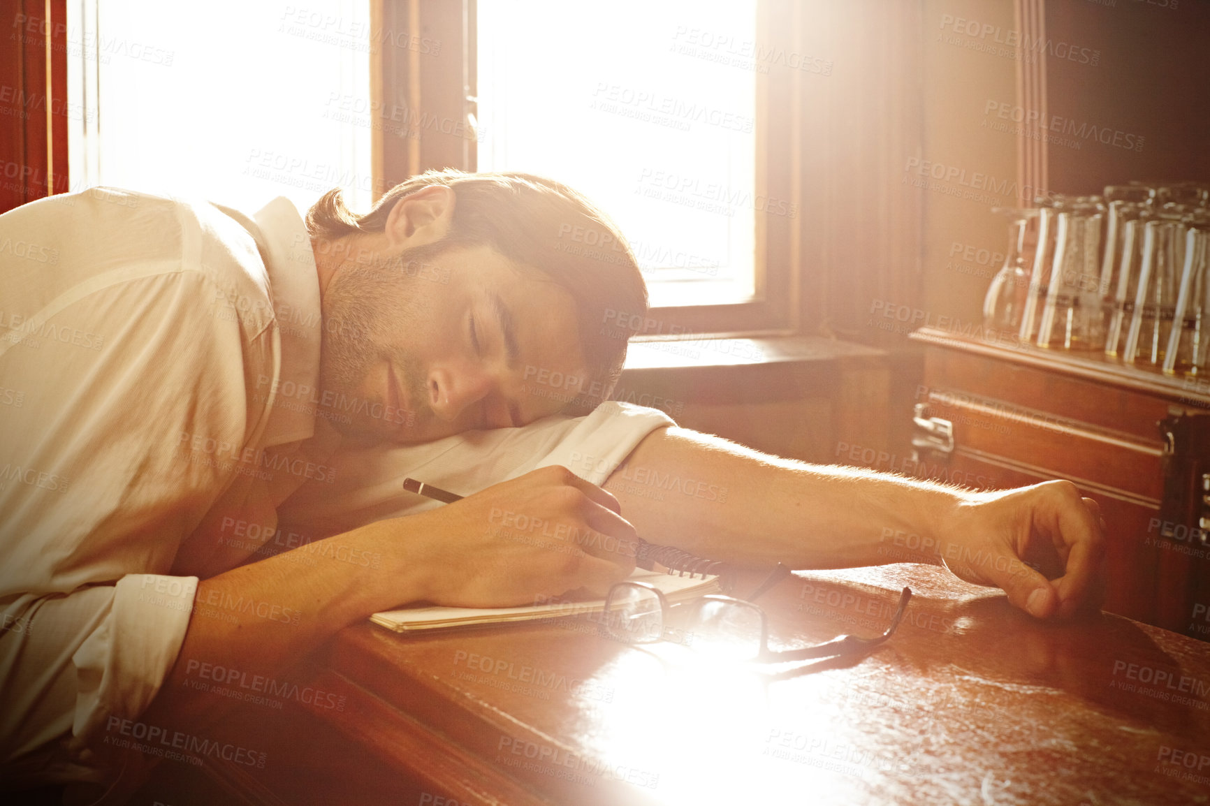 Buy stock photo Notebook, man and sleeping in bar or writing for journalist and media freelance career. Fatigue, exhausted and tired person, drink or author with glasses and notes or sunlight on table to nap or rest