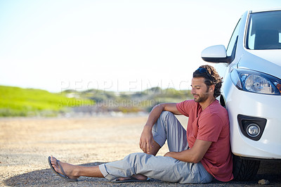 Buy stock photo A young man sitting on the road against the wheel of his car