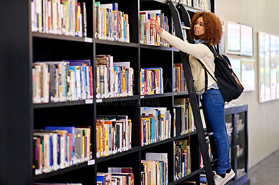 Buy stock photo Shot of a young woman reaching for a book from a bookshelf in a university library