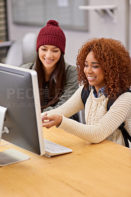 Buy stock photo Shot of two female students studying together at a computer in the library