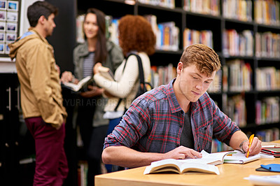 Buy stock photo Shot of a male student studying in a university library with his peers in the background